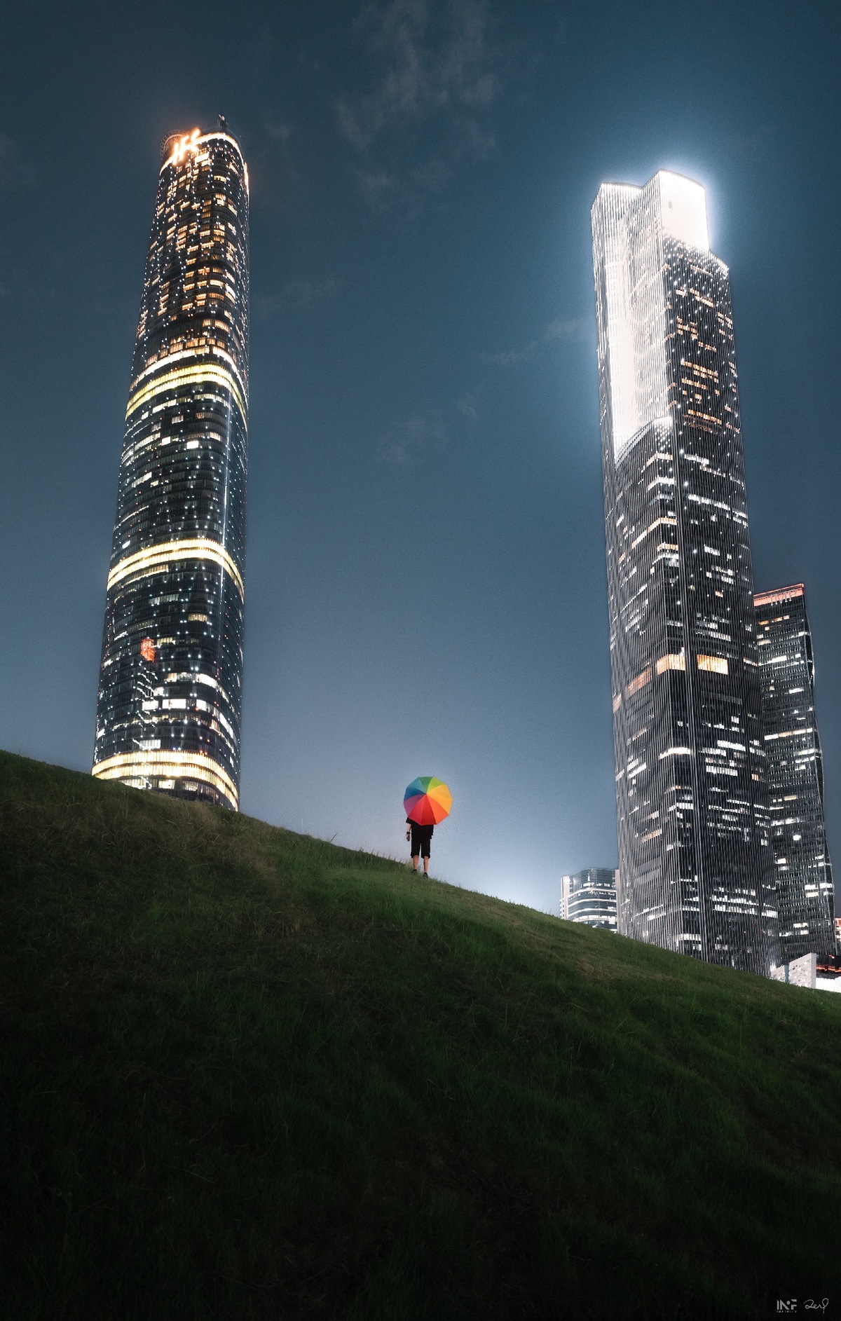 一个人站在草地上 手里拿着一个热气球和一只风筝 站在城市的高楼大厦前 夜晚。
