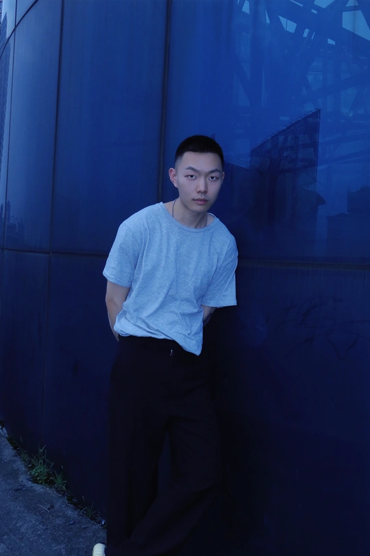一个年轻人站在一栋大楼旁边的蓝墙上