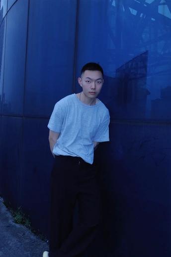 一个年轻人站在一栋大楼旁边的蓝墙上
