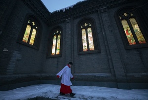 一位牧师穿过教堂彩色玻璃窗前的雪地