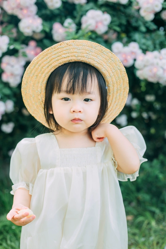 一个穿着白色连衣裙、戴着草帽的小女孩在花园里的画像