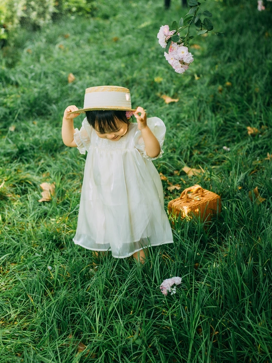 一个穿着白色连衣裙、戴着帽子的小女孩在花丛中行走