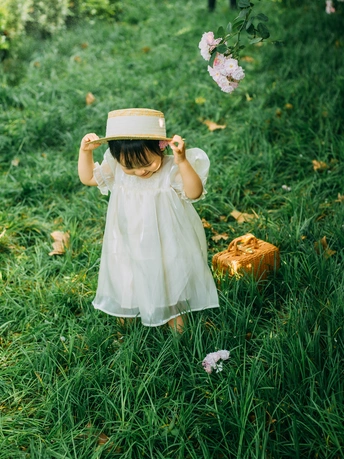 一个穿着白色连衣裙、戴着帽子的小女孩在花丛中行走