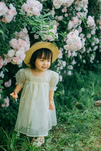 一个穿着连衣裙、戴着草帽的小女孩站在玫瑰园里