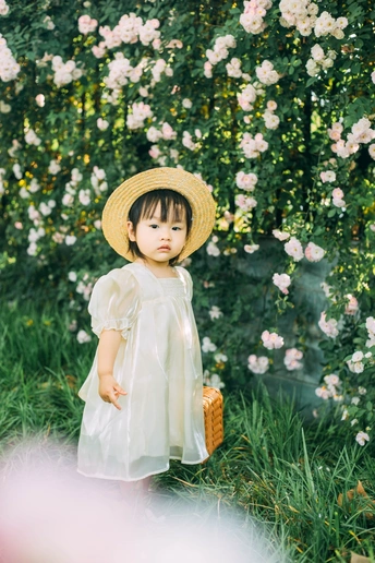一个穿着白色连衣裙、戴着草帽的年轻女孩站在一个有花的花园里