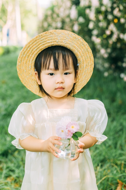 一个小女孩穿着连衣裙 戴着草帽 手里拿着一瓶粉红色的花在草地上的肖像