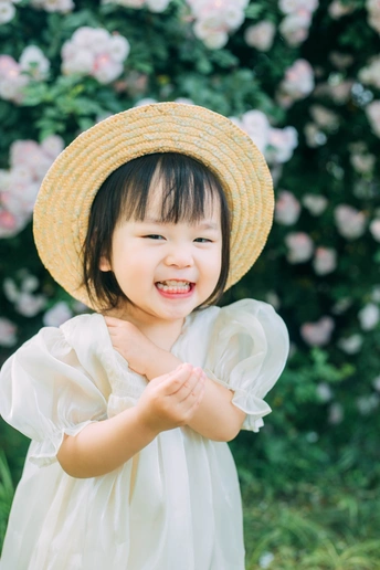 一个穿着白色连衣裙、戴着草帽的小女孩在花园里微笑的画像