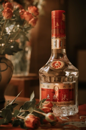 一瓶酒放在桌子旁边 旁边有一束红色的玫瑰花。