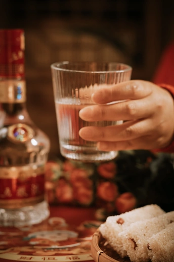 一个人手里拿着一杯酒 背景有一个盘子和一瓶酒精饮料。