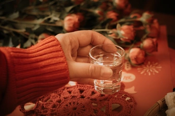 一位女性手持一杯水 放在桌子上 周围有花。