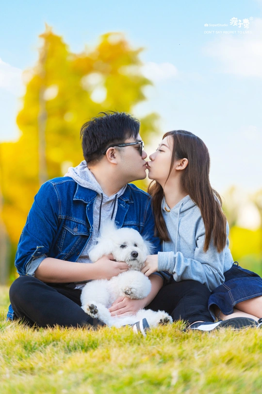 年轻夫妇在草地上亲吻 带着他们的白色小狗在公园里