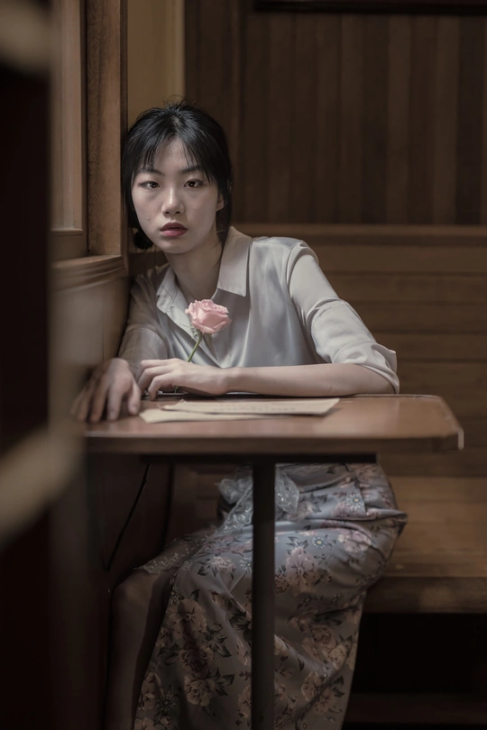 一个坐在木桌旁的年轻女人 桌上放着一朵粉红色的花