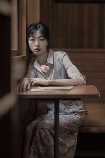 一个坐在木桌旁的年轻女人 桌上放着一朵粉红色的花