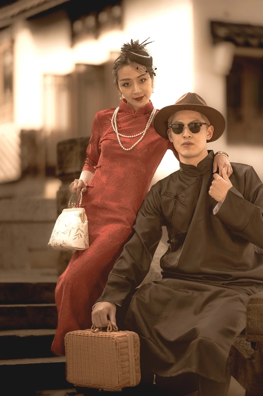 一名身穿红色连衣裙、戴着帽子的年轻男子与一名提着行李箱的年轻女子合影