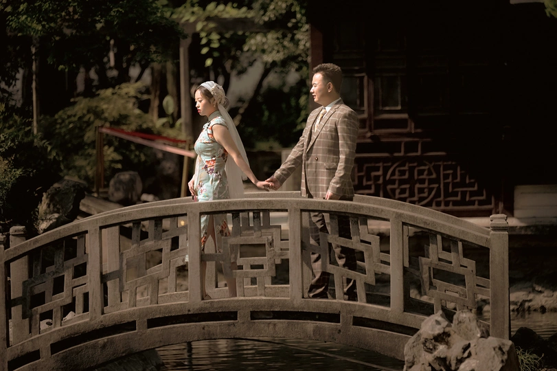 一男一女手牵着手走过一座小池塘上的木桥