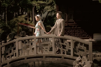 一男一女手牵着手走过一座小池塘上的木桥