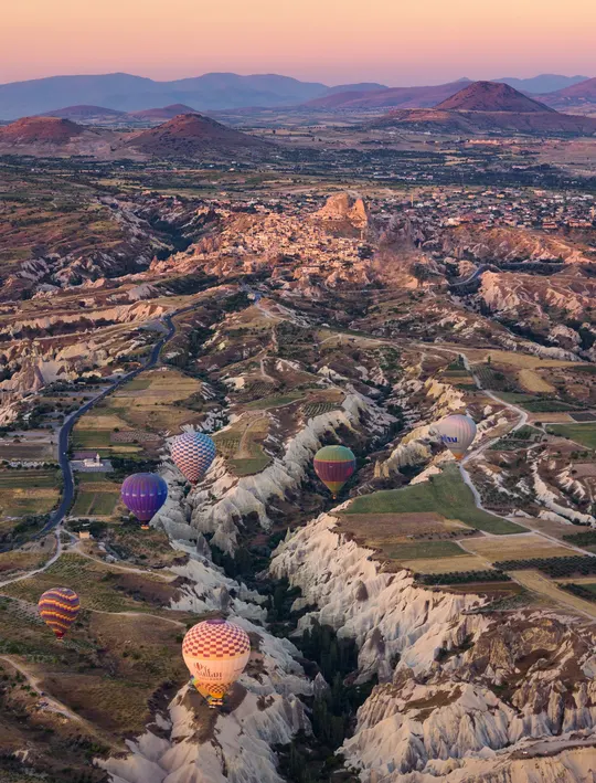 热气球在日出时分飞越山谷 山谷两侧有山脉和远处的城市。
