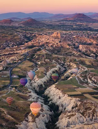 热气球在日出时分飞越山谷 山谷两侧有山脉和远处的城市。