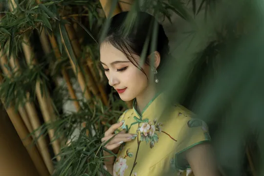 一位穿着黄色衬衫和绿色雨伞的年轻女子站在竹林和绿色植物、花丛前。