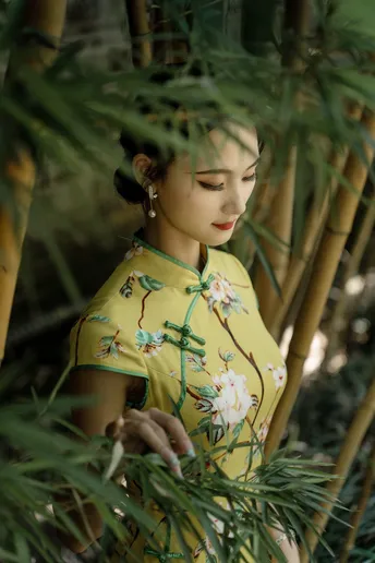 一位穿着中国传统裙子的年轻女子站在竹林中 手持一把伞和一株绿色植物在她身后。