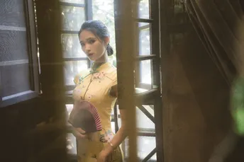 一位穿着黄色连衣裙的年轻女子 holding a door and looking out a wi