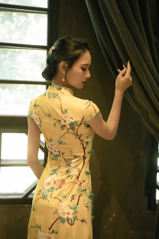 一位穿着黄色花卉裙子的年轻女子站在窗户前