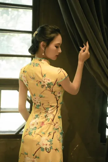 一位穿着黄色花卉裙子的年轻女子站在窗户前