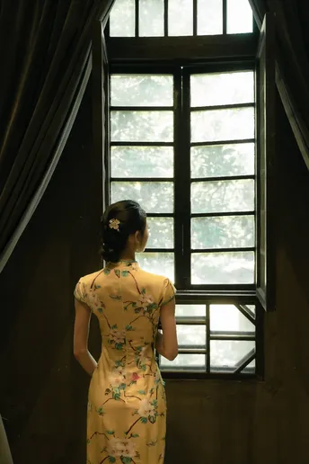 一位穿着黄色连衣裙的女人站在窗前 窗帘垂下。