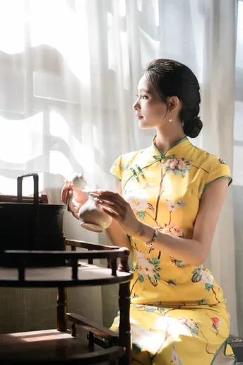 一位穿着黄色连衣裙的女人坐在桌子旁 桌子上放着一个碗。