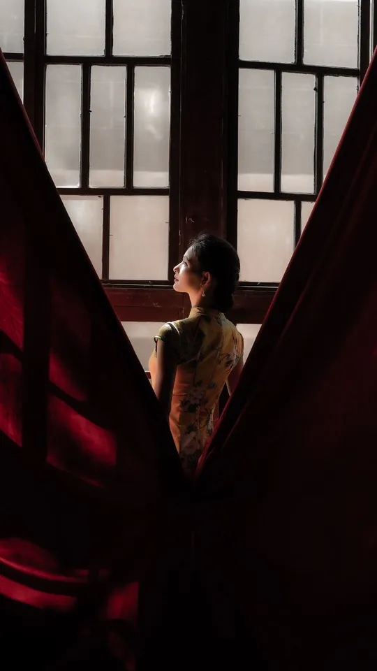 一位年轻女子站在一扇打开的窗户前 窗帘是红色的。