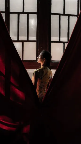 一位年轻女子站在一扇打开的窗户前 窗帘是红色的。