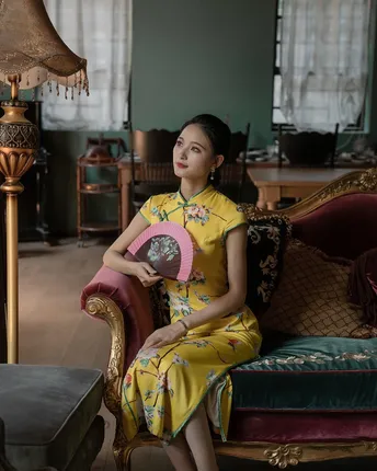 一位穿着黄色连衣裙的年轻女子坐在椅子上 手里拿着一把扇子。