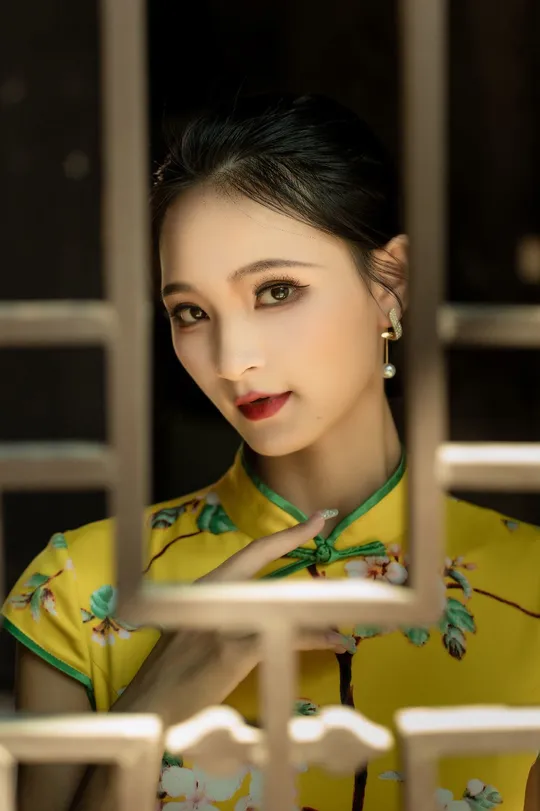 一位穿着黄色传统裙子的女孩站在窗前