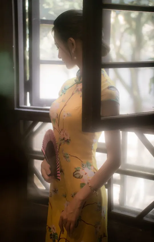 一位穿着黄色连衣裙的年轻女子站在窗户前照镜子