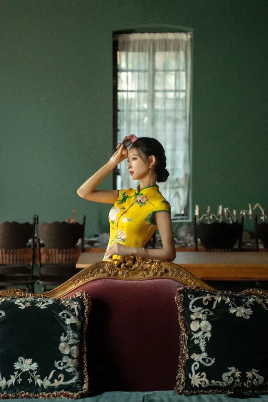 一位穿着黄色传统裙子的年轻女子坐在一个带有镜子的房间里的一张沙发上。