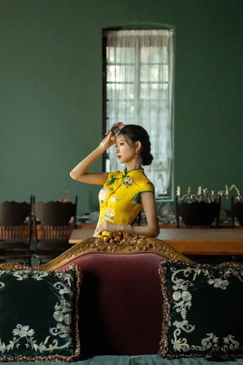 一位穿着黄色传统裙子的年轻女子坐在一个带有镜子的房间里的一张沙发上。