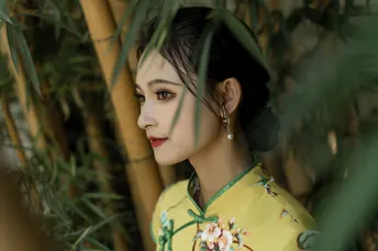 一位穿着黄色连衣裙的年轻女子站在绿竹前
