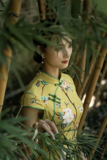 一位穿着中国传统裙子的年轻女子站在竹林中 手持雨伞和一株绿色植物。