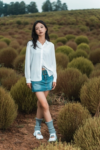 一位年轻女子穿着一件白色衬衫站在一片灌木丛中
