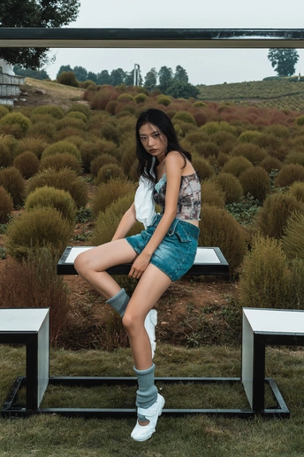 一个穿着靴子的年轻女子坐在白色长凳上 双腿交叉在草地中。