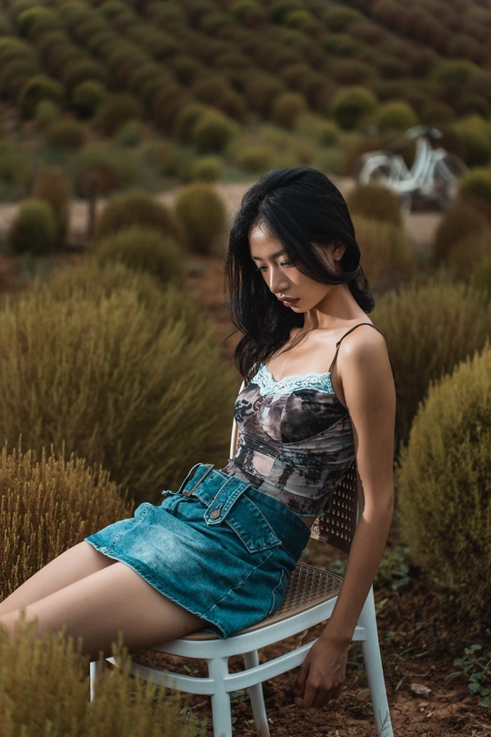 一位坐在白色椅子上、在灌木丛中摆姿势的美丽年轻女子