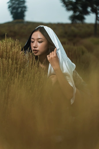 一个戴头纱的年轻女孩坐在茂密的草地上