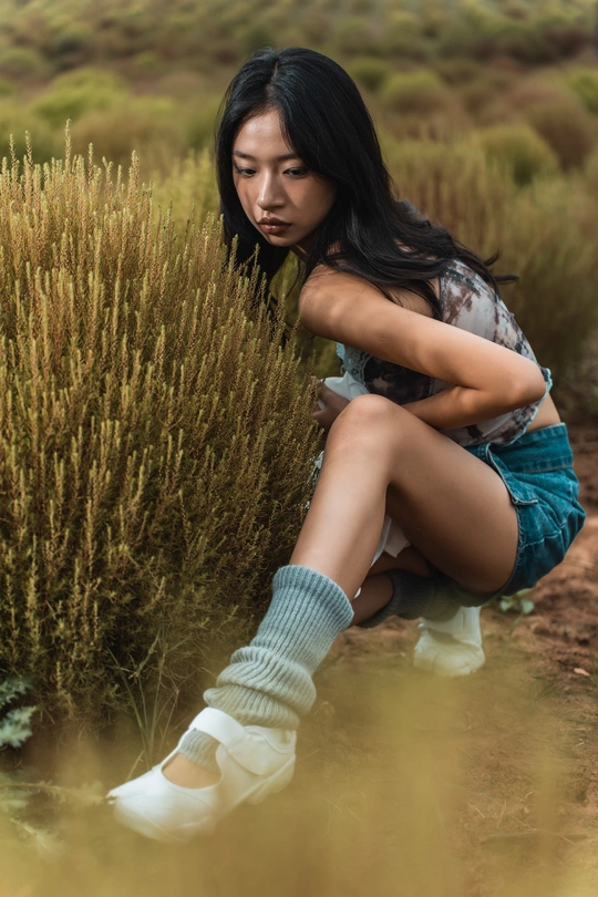 一位年轻女子穿着袜子坐在草地上的灌木丛中