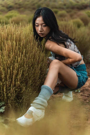 一位年轻女子穿着袜子坐在草地上的灌木丛中