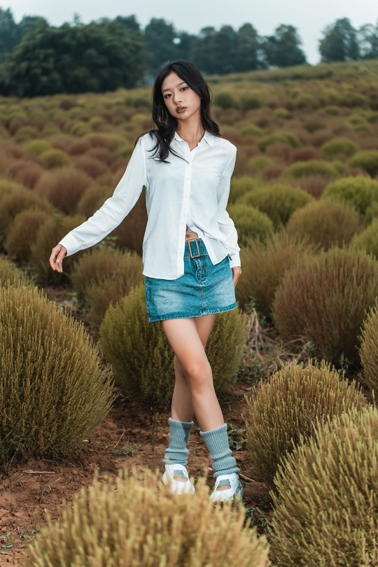 一位穿着白衬衫和裙子的年轻女子穿过一片灌木丛。