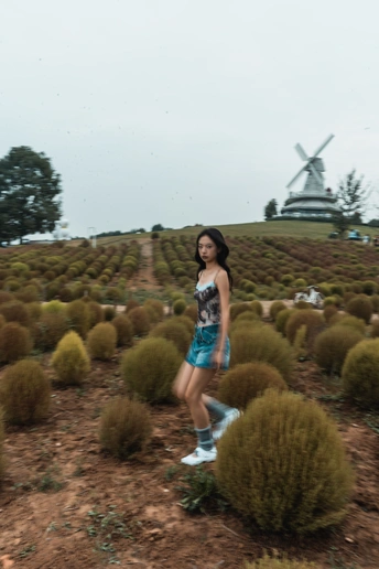 一位年轻女子站在植物田中 背景中有风车。