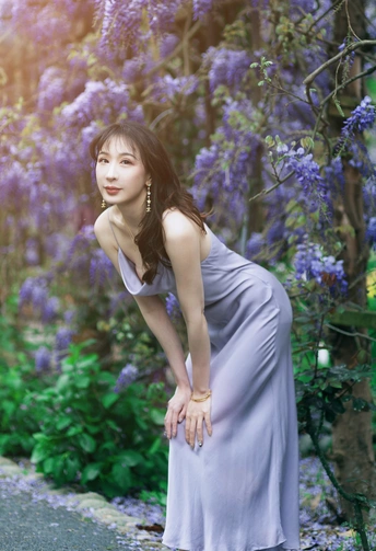 一位穿着长裙的美丽年轻女子站在一个开满紫花的花园里