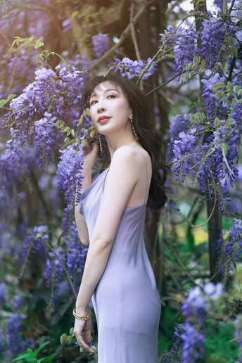 一位穿着蓝色连衣裙的美女站在紫花前面