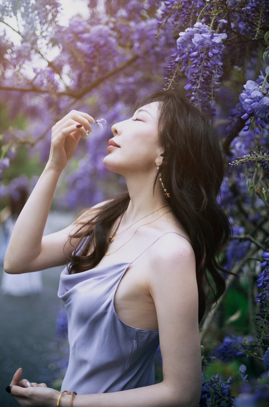 一位穿着蓝色连衣裙的年轻女子在吹紫色花朵