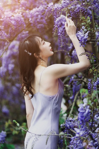 一位穿着蓝色连衣裙的年轻女子站在一片紫花环绕的田野中
